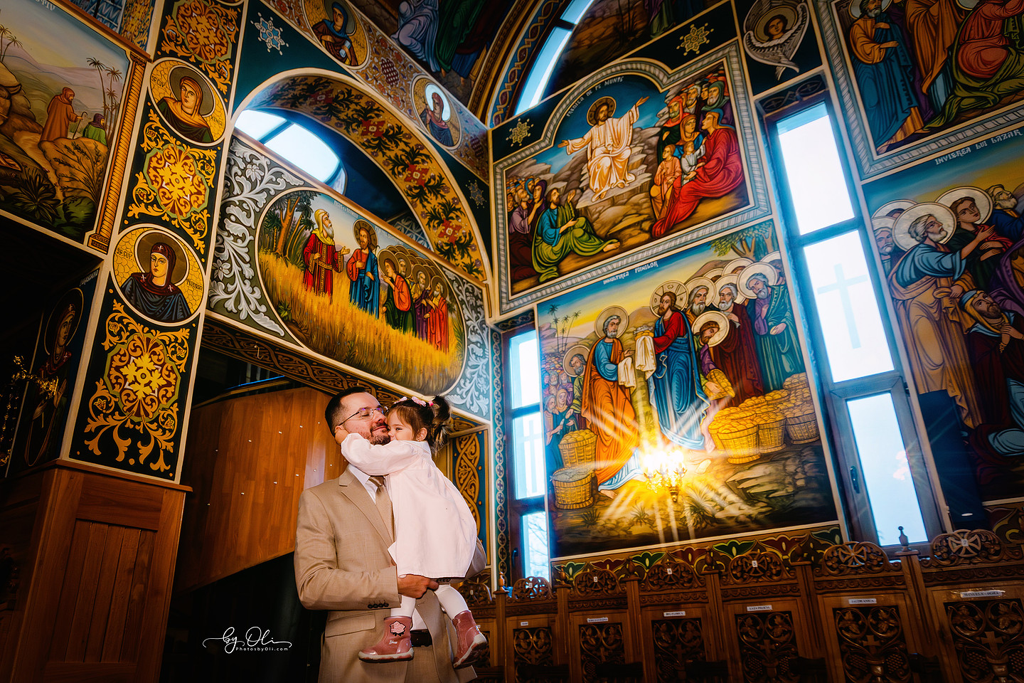 Tata si fiica intr-un moment de conectare in Biserica Sf. Nicolae Timisoara, fotografie artistica de familie realizata de fotograf profesionist de botez, lumina si picturi bisericesti spectaculoase, atmosfera calda, poveste vizuala premium, fotografie botez Timisoara, imagini emotionale in biserica deosebita.