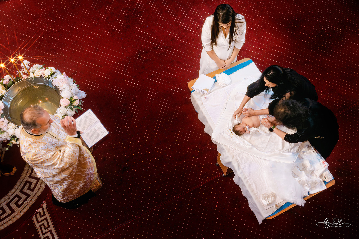 Prima imbracare a copilului dupa botez, fotografie artistica din Biserica Sf. Nicolae Timisoara, surprinsa de fotograf profesionist de botez din Timisoara. Cadru vazut de sus cu preotul, cristelnita, trusou si familie, poveste vizuala premium, moment emotional al slujbei ortodoxe.