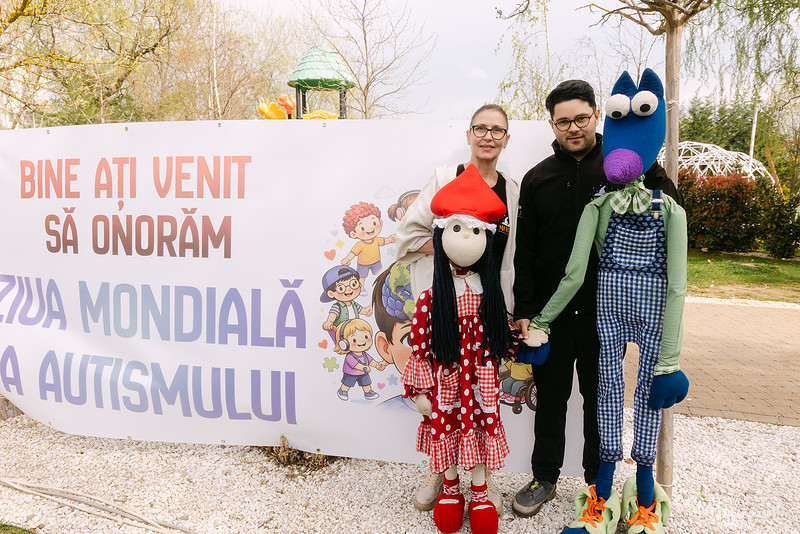 Doi adulti pozand langa papusi gigant la evenimentul Ziua Mondiala a Autismului, Teatrul Merlin Timisoara, fotografie de eveniment Photos by Oli